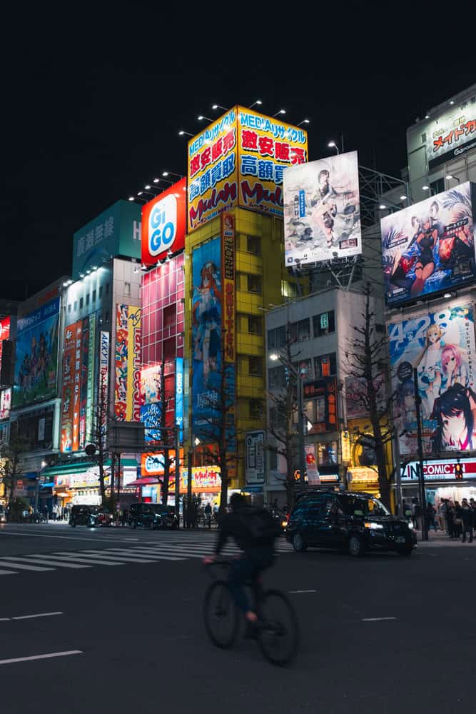 Grattacieli con neon colorati ad Akihabara con una persona che passa in bici davanti