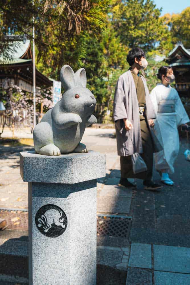Una coppia passeggia nel tempio dei conigli a Kyoto dietro a una statua di un coniglio