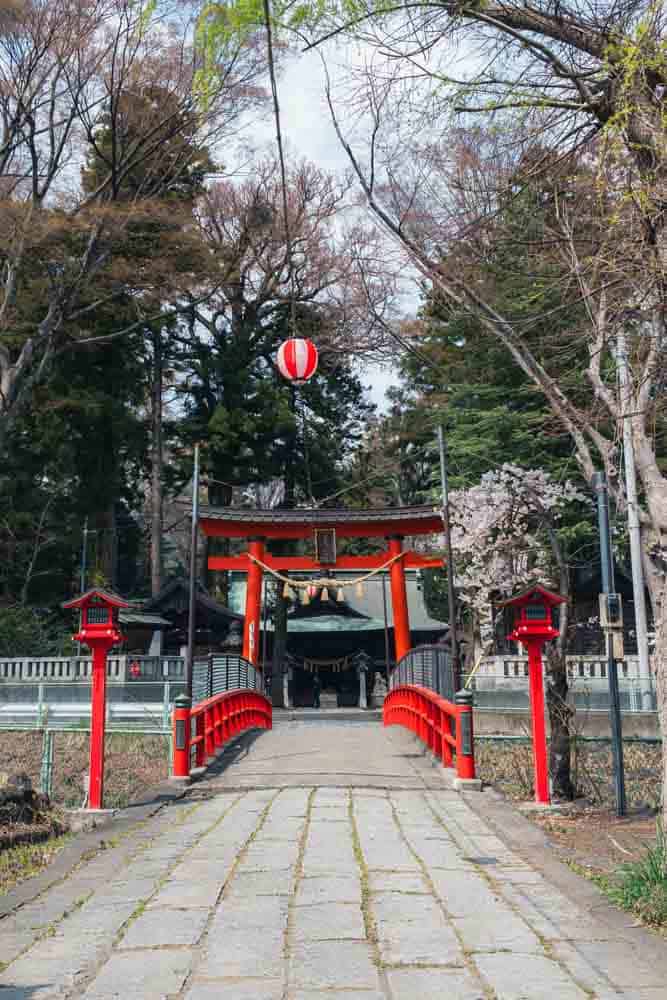 Ingresso di un tempio a Fujiyoshida con un torii rosso all'ingresso dopo il ponte