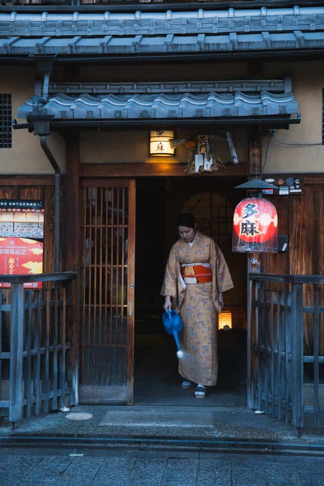 Una ragazza che lava l'ingresso di un locale di Kyoto nel quartiere Gion