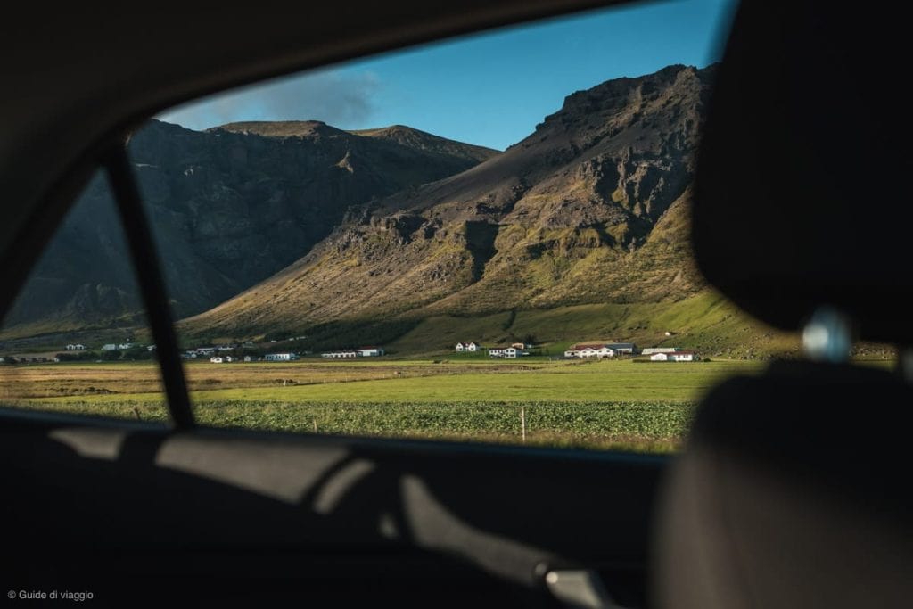 Panorama di alcune case islandesi di fronte a una montagna viste dal finestrino dell'auto