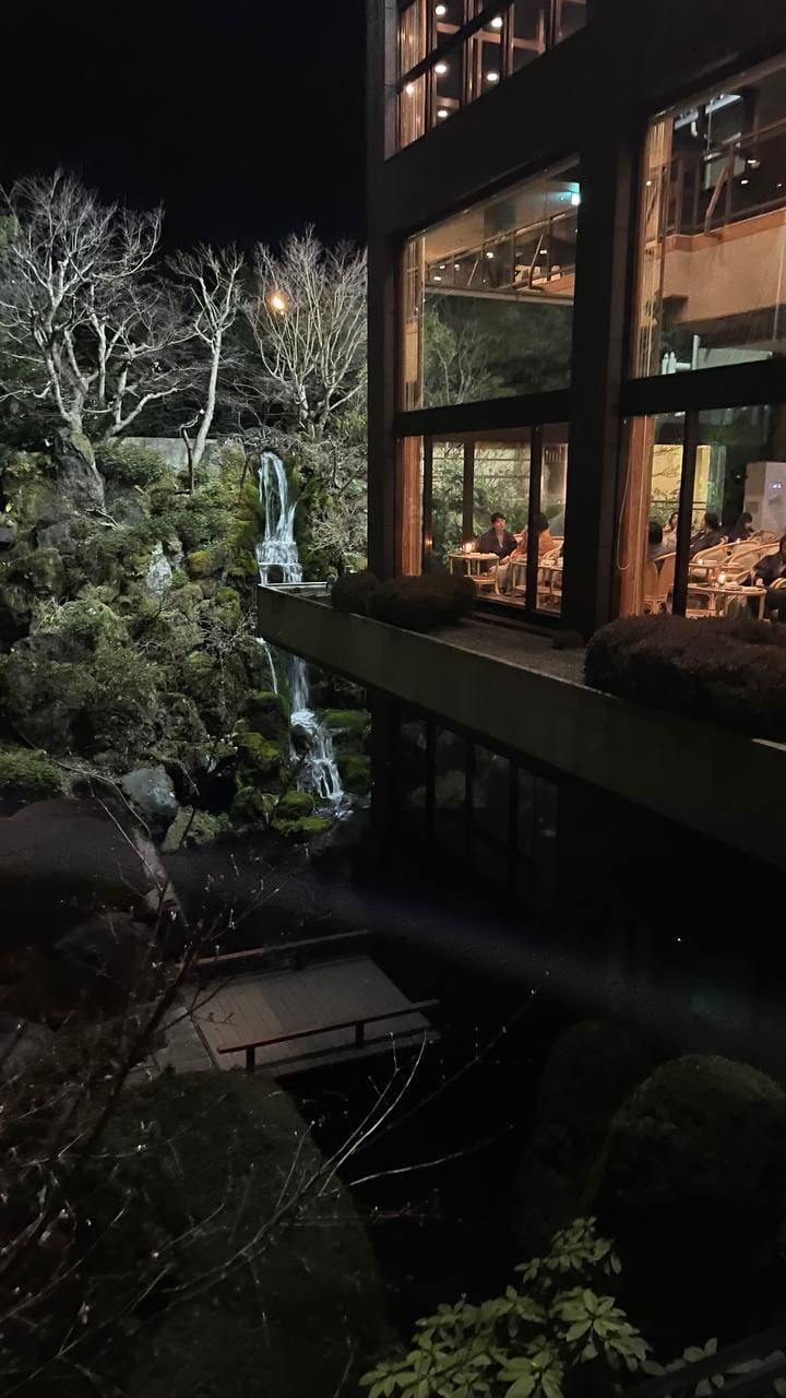 Giardino dell'hotel Kaneyamaen di sera con una cascata e le enormi vetrate del ryokan illuminate